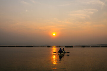Asian couple canoeing in the river in the morning with beautiful sunrise.