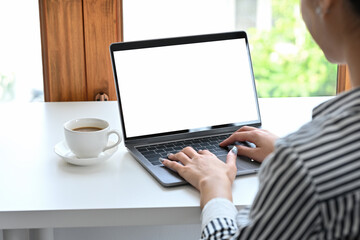Fototapeta premium Close up shoulder view lady typing something by using blank screen laptop computer on a desk with a coffee cup in the workplace, business and financial concepts.