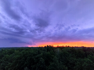 Bright orange sunset over the treetops in the forest. Beautiful sundown over the dark woods.