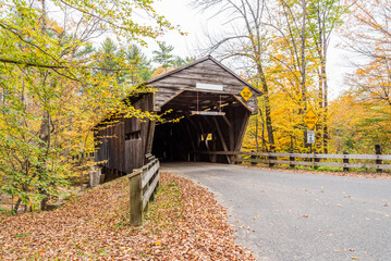 Old wooden covered bridge along a forest road in New England on a cloudy autumn day