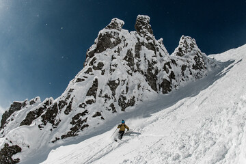 freeride skier riding down on steep snowy mountain on a sunny day.