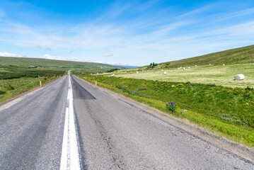 Deserted straight stretch of a country road in Iceland on a clear summer day. Snow-capped mountains are visible in background.