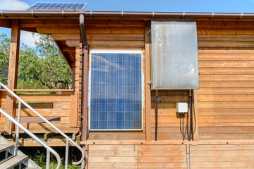 Solar panels on the external wall and on the roof of a wooden cabin on a sunny summer day. Sustainable energy concept.