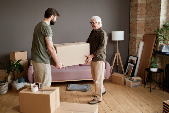 Horizontal shot of young man helping his father with moving to new apartment carrying big heavy box together