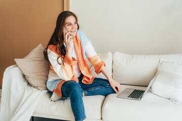 Obraz premium Confident business woman calling by phone while working on a laptop at home in a cozy living room.