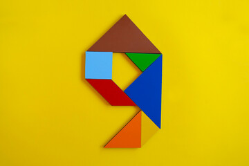 Colorful number 9 made with tangram toy, colored tangram number nine isolated on yellow background,...