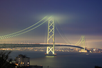 Traffic moves along suspension bridge lit up on cloudy night