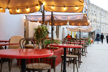 Fototapeta na wymiar Street cafe with red tables and vintage chairs outdoor, decorated with festive lights