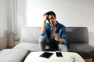 Fototapeta premium Upset man holding a credit card, thinking of calculator accounting costs, charges, taxes, and debt for paying bills looking worried and stressed about paying online problem form laptop and cell phone