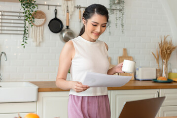 Beautiful young asian woman working at the kitchen room, drinking coffee.