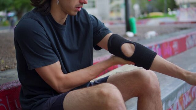 young latino man at a skate park putting on protective elbow pads. 4k video