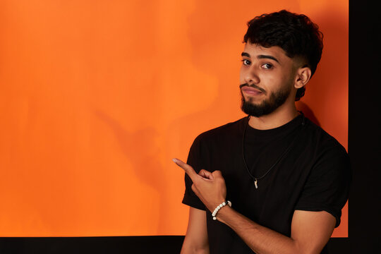 hombre joven latino con expresion incredula en la cara se&ntilde;alando con las manos en un fondo naranja con negro