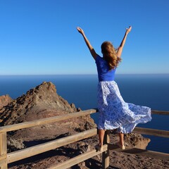 Swobodna kobieta ubrana w długą spódnicę w wietrzny dzień ciesząca się pięknym widokiem oceanu na wyspie Fuerteventura - obrazy, fototapety, plakaty