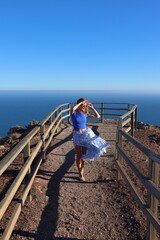 Radosna kobieta w rozwianej spódnicy spaceruje po moście na tle oceanu na wyspie Fuerteventura - obrazy, fototapety, plakaty