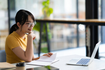 Fototapeta premium Portrait of Asian businesswoman with laptop writes on a document at her office