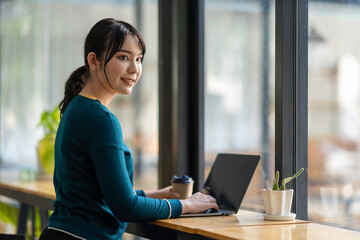 Happy young Asian businesswoman using a laptop computer doing online shopping at the cafe. Smiling beautiful Asian woman sitting and working at