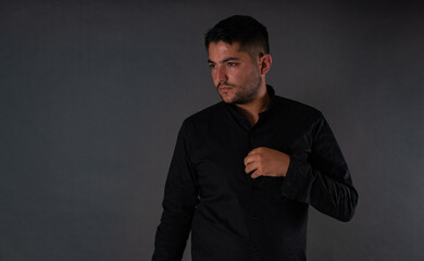 A man in a black shirt, with his hands on his chest and posing on a gray background looking to the side. Emotions, joy and fun of men.