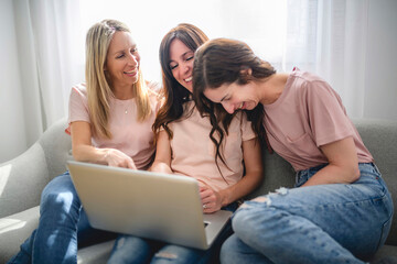 smiling best girl friends blond and brunette sit on sofa with laptop
