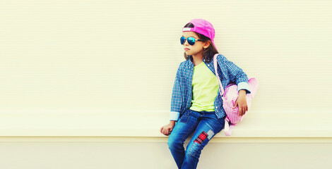 Portrait of little girl child wearing baseball cap with pink backpack on city street background