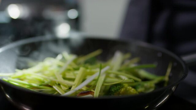 Close up shot of stirring leeks, broccoli and potato in frying pan with tweezers while cooking veggies