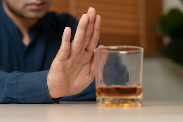 Alcoholism, depressed asian young man refuse, push out alcoholic beverage glass, drink whiskey, sitting alone at night. Treatment of alcohol addiction, having suffer abuse problem alcoholism concept.