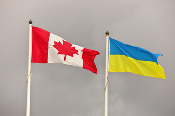 Canada and Ukraine national flags waving in wind against cloudy sky. Ukrainian and Canadian Flag