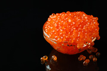 Glass bowl with delicious red caviar on black background. Space for text