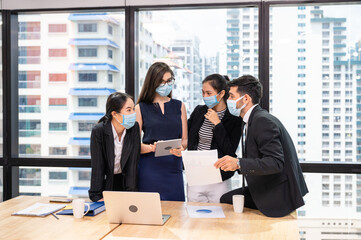 Multiethnic business team wearing face mask during business meeting in new normal office. Diverse corporate colleagues brainstorming with technology device
