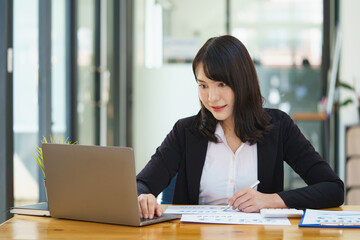 Portrait of smiling beautiful business asian woman working in office use computer to analysis accounting chart and tax.