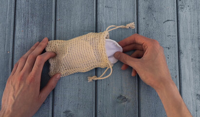 woman hand pulls reusable organic cotton pad out of knitted eco bag on blue wooden background. eco-friendly make-up remover. © kotograf
