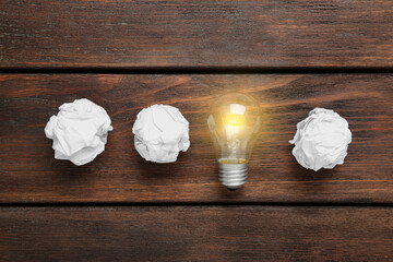 Crumpled paper balls and lamp bulb on wooden table, flat lay. Idea concept