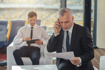 Portrait of mature businessman calling by phone while sitting in the office