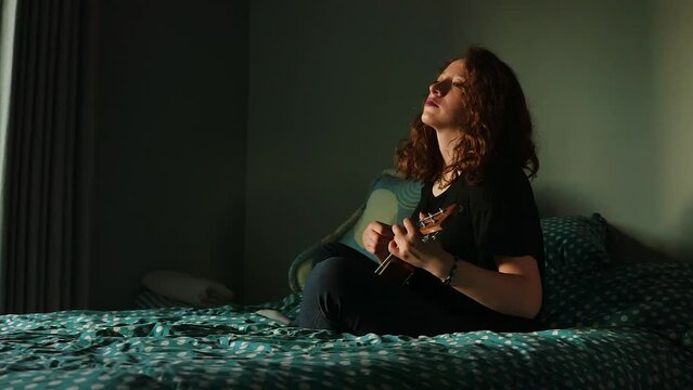 Mujer tocando el ukulele y cantando en su habitaci&oacute;n. Concepto de musica.