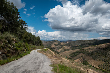 Estrada com curvas rodeado por montes e montanhas e o céu parcialmente nublado