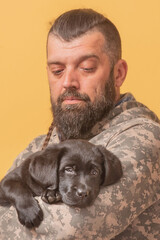 Man in military clothes with a Labrador Retriever puppy in his arms. Man and dog.