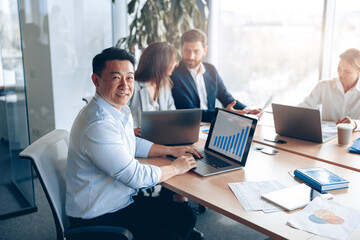 Portrait of smiling asian businessman working on a laptop during a meeting with a team. Business concept