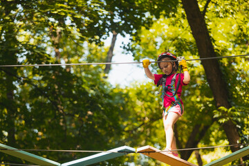 The concentrated girl carefully overcomes obstacles in the rope park