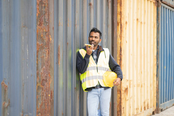 Indian industrial worker man talking on his smartphone at shipping cargo terminal port - logistics workers concept -