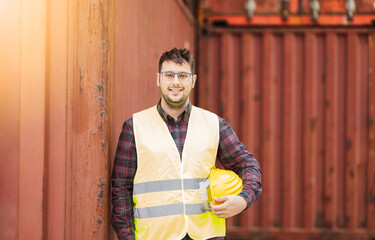 Caucasian man looking at camera, cargo port operator smiling with protective helmet and reflective vest - work in port logistics -