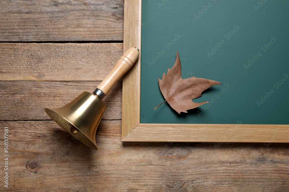 Wall mural Golden school bell and green chalkboard with autumn leaf on wooden table, flat lay