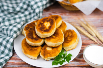 Delicious fried homemade pies with potatoes and meat with sour cream on the kitchen wooden table. Close-up.