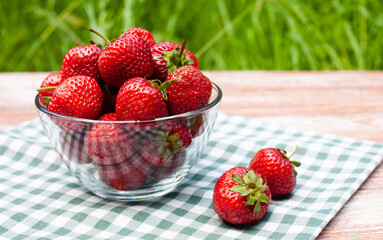 Fresh juicy strawberry in glass bowl on a wooden table outside. Close-up. Place for text.