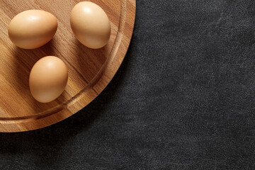Eggs chicken on wooden board, on dark background, top view, space to copy text.