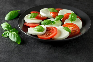 Caprese, Italian dish of mozzarella tomatoes and basil on  dark plate, selective focus.