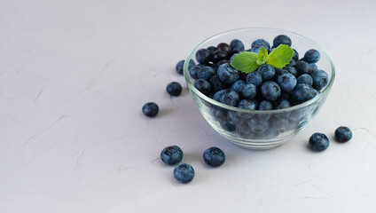 Freshly picked blueberries in a glass bowl on grey background. Close-up. Place for text.