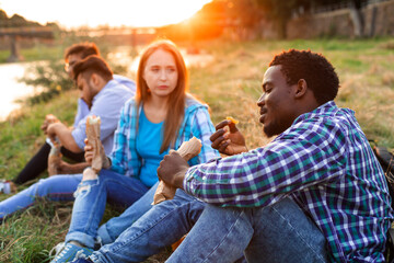 The group of young diverse people eating fastfood on nature