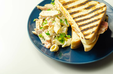 White bread with beechwood smoked bacon, egg, mayonnaise, and tomato served with Caesar pasta with parmesan cheese on the blue plate