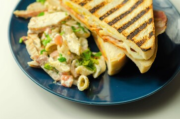 White bread with beechwood smoked bacon, egg, mayonnaise, and tomato served with Caesar pasta with parmesan cheese on the blue plate
