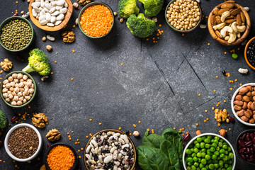 Vegan protein source. Food frame. Legumes, beans, nuts, vegetables and seeds. Top view on black stone table.