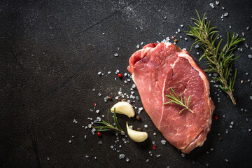 Raw meat. Fresh steak, pork steak with herbs and spices at black background. Top view with space for text.